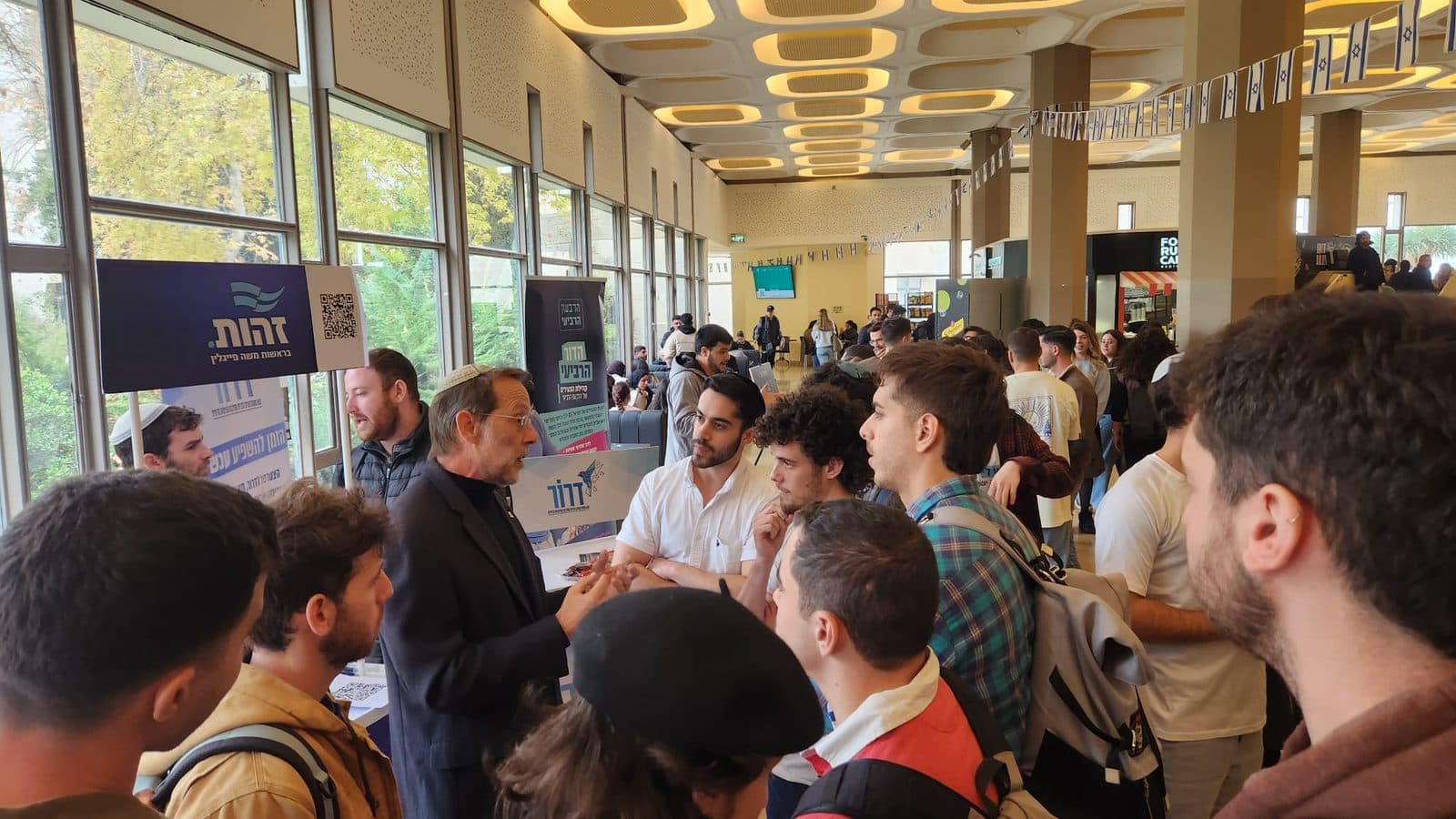 משה פייגלין משוחח עם סטודנטים בדוכן זהות בקמפוס, קהל סטודנטים צעיר סביבו