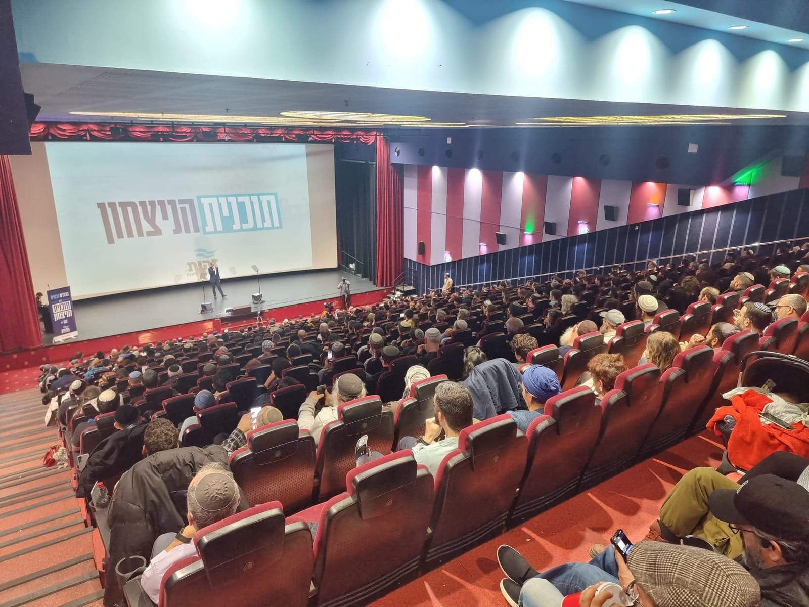 A cinema hall filled with hundreds of participants at Zehut's "Victory Plan" conference, the conference name projected on the screen